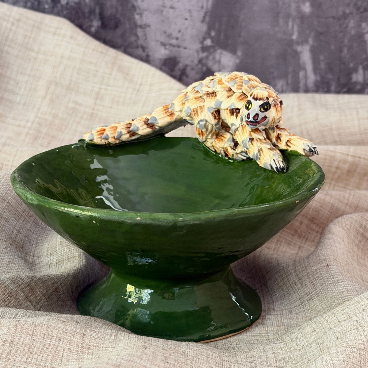 forest green ceramic mini raised bowl with a hand sculpted pangolin moving across the rim, long tail trailing behind