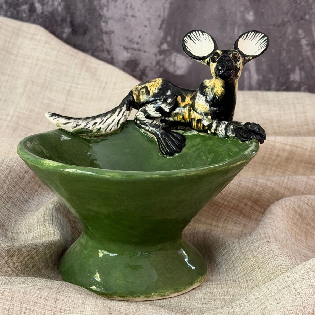 forest green ceramic mini raised bowl with a hand painted african wild dog on the rim, nose down as if catching a scent