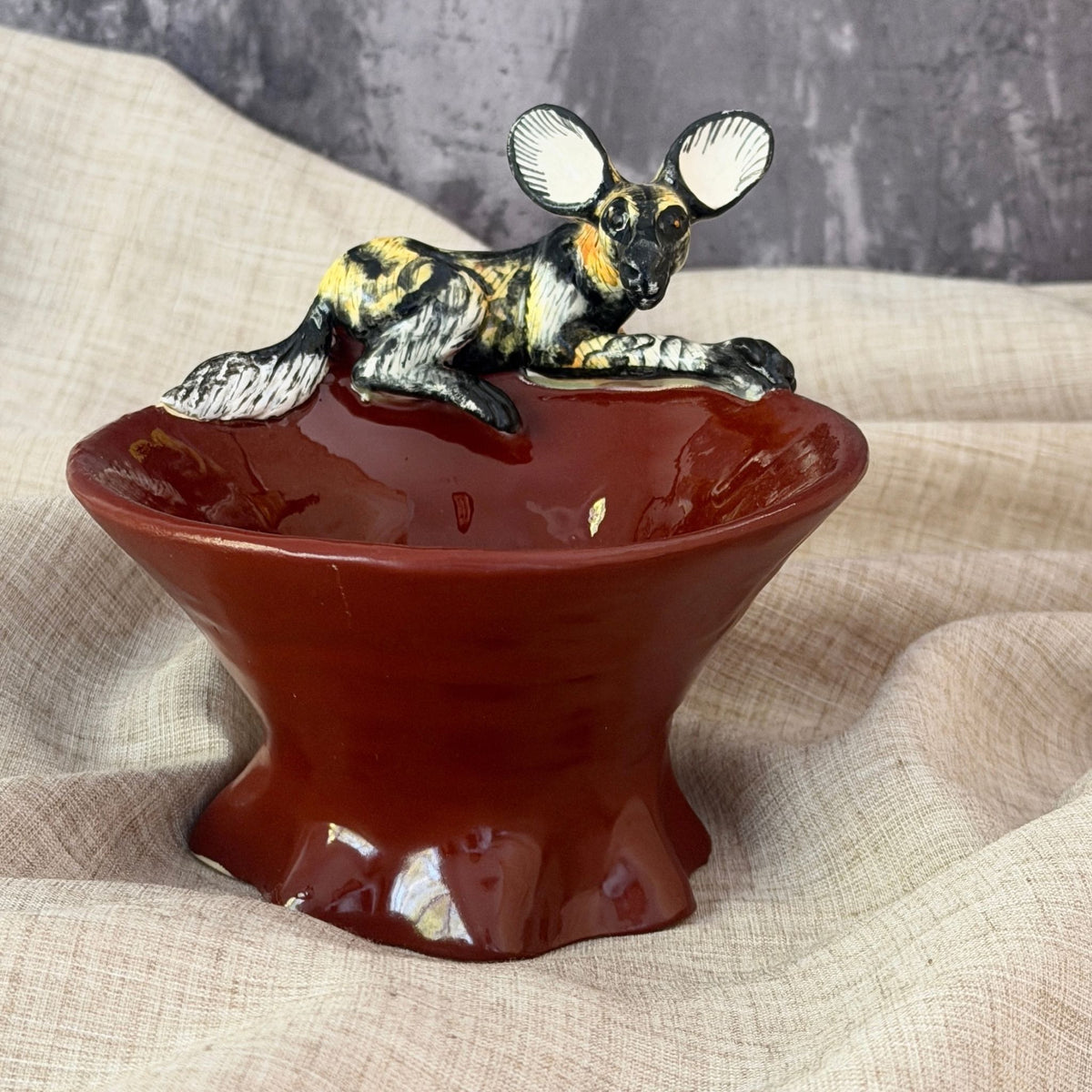 rooibos red ceramic mini raised bowl with a hand painted african wild dog resting on the rim, ears up