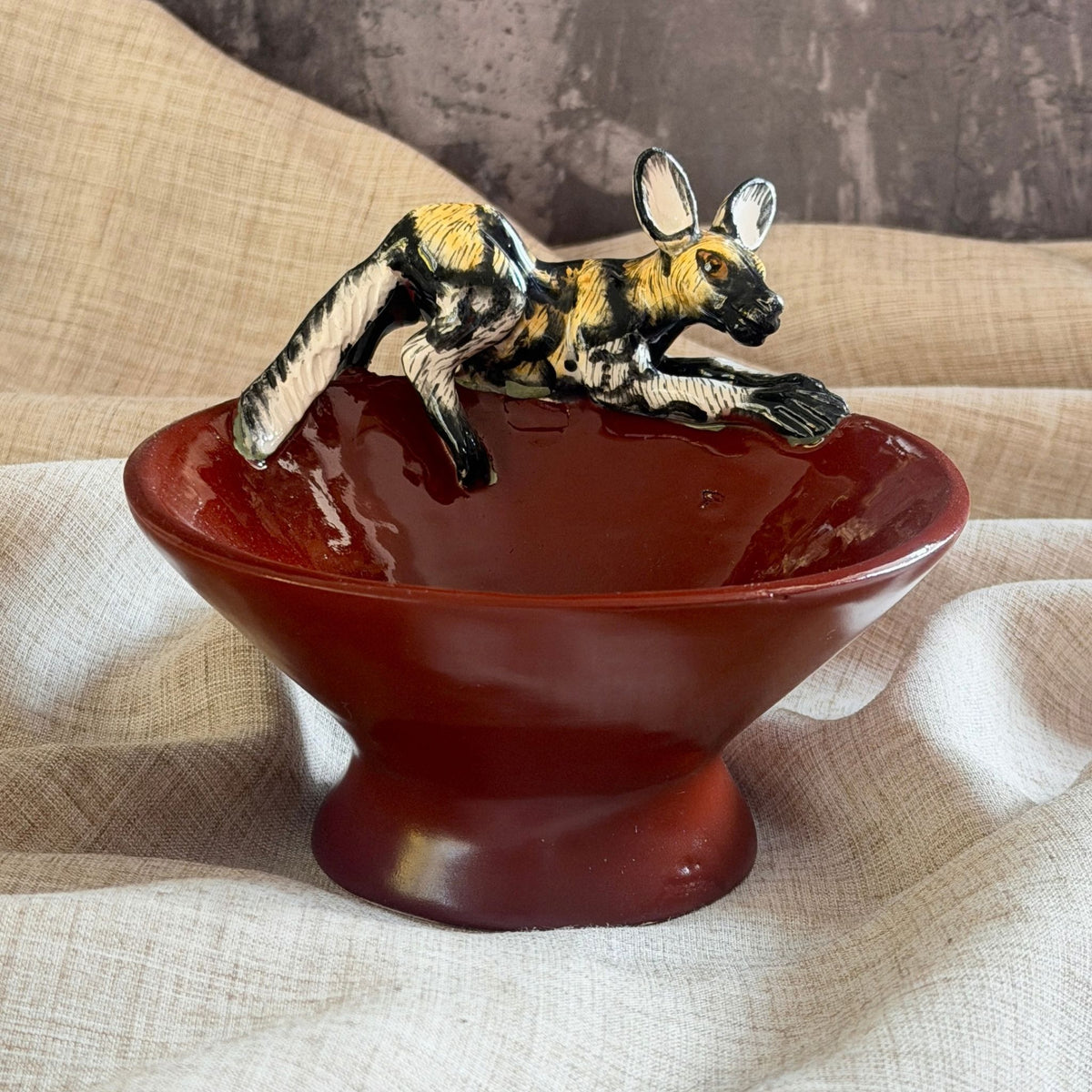 rooibos red ceramic mini raised bowl with a hand painted african wild dog stretched low across the rim, paws reaching forward