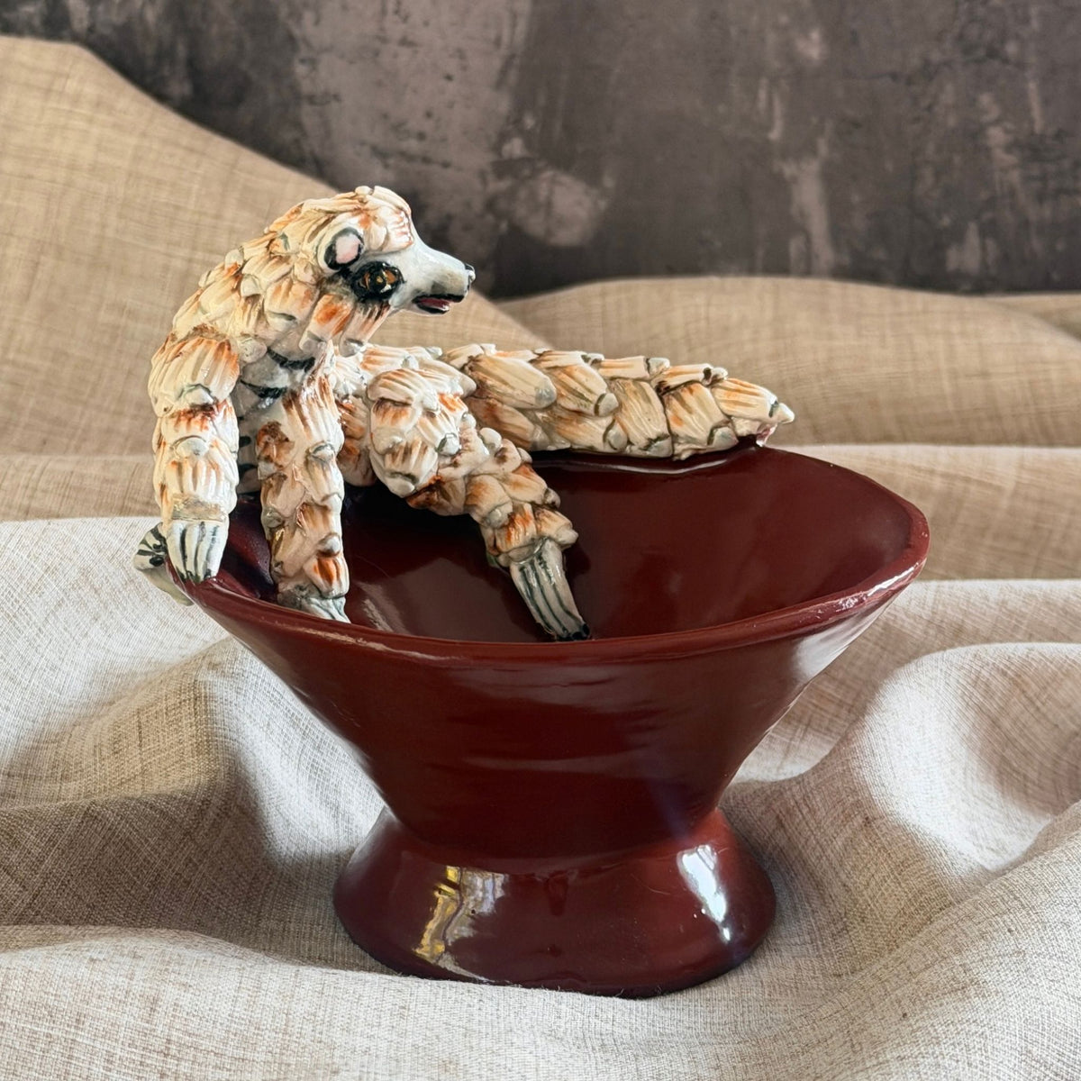 rooibos red ceramic mini raised bowl with a hand sculpted pangolin reaching across the rim, each scale tipped in black