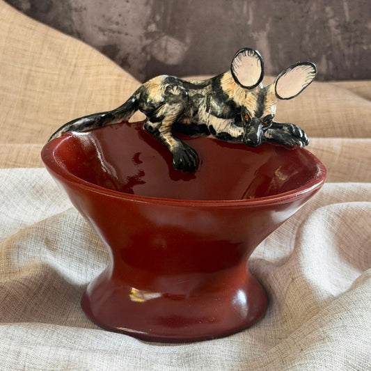 rooibos red ceramic mini raised bowl with a hand painted african wild dog leaning in over the rim with its head lowered